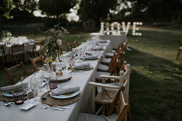 Fototapeta na wymiar Mesa para celebración de bodas. Mesa alargada ubicada en la pradera sobre el pasto verde, al final de la mesa hay un cartel luminoso que dice amor.