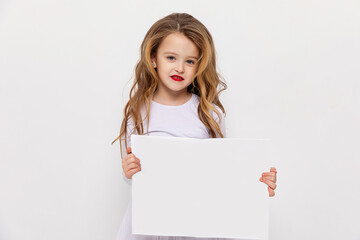 Cute little fashion girl with curly hair and red lips holding a white blank paper with copy space on white background. white sheet mock up