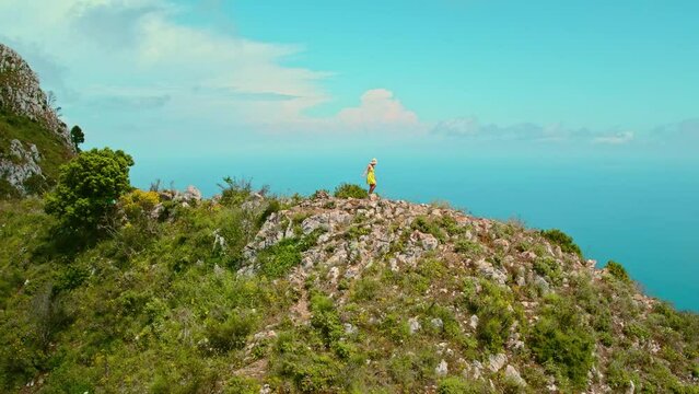 Solo Traveler Contemplating Sea from Rocky Summit. A lone woman walking along coastline, overlooking the vast expanse of the blue sea and sky. Capri Island, Italy.