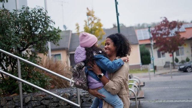 Female nurse, doctor picking up small daughter from kindergarten, preschool, embracing in front school building. Work-life balance of healthcare worker as parent and partner.