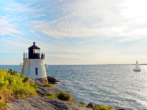 Castle Hill Lighthouse in summer, a beautiful and famous New England light house, Newport, Rhode Island, USA with a sailboat in the distance in Narragansett Bay.