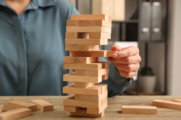 Playing Jenga. Woman removing block from tower at wooden table indoors, closeup