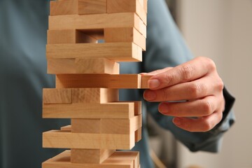 Playing Jenga. Woman removing wooden block from tower indoors, closeup