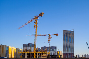 Yellow tower cranes on construction site against the backdrop of city skyline and blue sky for illustrating construction, urban development, and progress