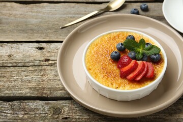 Delicious creme brulee with berries and mint in bowl on wooden table, closeup. Space for text