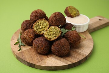 Delicious falafel balls, arugula and sauce on green background
