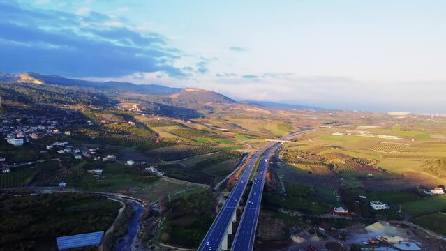 Drone captures traffic on highway crossing green fields under a blue sky. Aerial footage depicts the essence of highway, road trip. Explore vast landscapes from perspective of highway, road trip