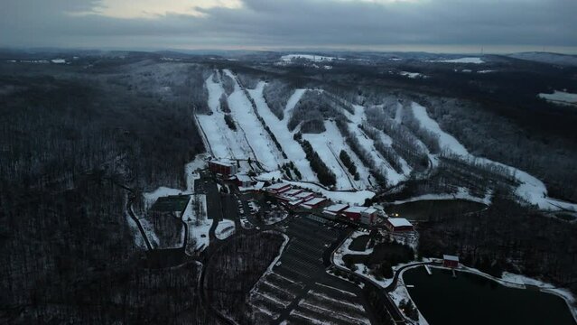 Aerial footage of buildings and tennis pitches on snowy Poconos landscape under cloudy sky at sunset