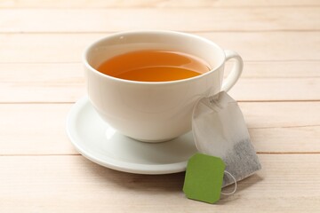 Tea bag and cup of hot beverage on light wooden table, closeup