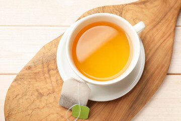 Tea bag and cup of hot beverage on light wooden table, top view
