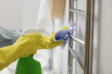 Woman cleaning heated towel rail with sprayer and rag, closeup - obrazy, fototapety, plakaty