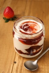 Tasty yoghurt with jam, spoon and strawberry on wooden table, closeup