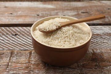 Raw basmati rice and spoon in bowl on wooden table