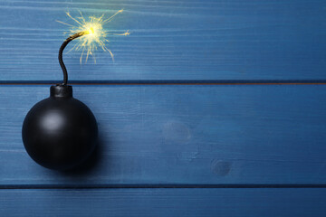 Old fashioned black bomb with lit fuse on blue wooden table, top view. Space for text