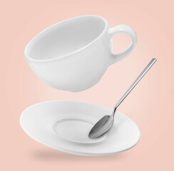 Spoon, cup and saucer falling on pale pink background