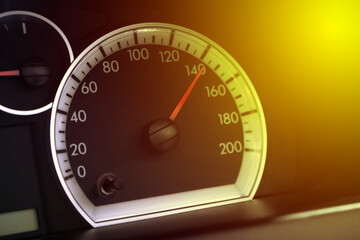 Speedometer on car dashboard under yellow light, closeup