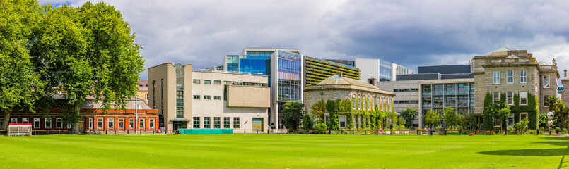 Trinity College Dublin campus with green field and buildings in the background, Ireland. The image features a view of the modern college. The college's historic buildings are in the background