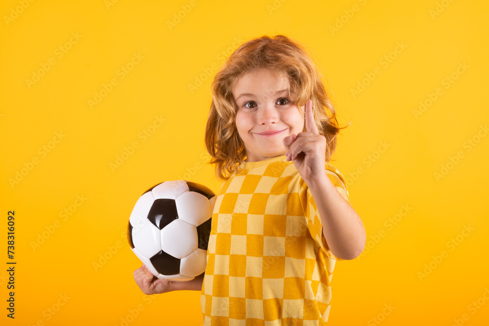 Wall mural Child boy hold classic soccer ball isolated on yellow studio. Kid holding football ball in studio. Kid playing with ball. Sport, soccer hobby for kids. Little soccer player posing with soccer ball.