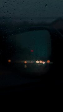 A dark, cinematic, blurry image in the rearview mirror on a rainy day