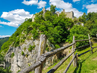 Fototapeta na wymiar Wooden fence with panoramic view of rock castle Rabenstein in Sankt Paul im Lavanttal, Wolfsberg, Carinthia, Austria. Sightseeing of ancient ruins of landmark in Austrian Alps. Fortress built on rock