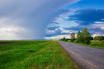 thunderstorm and heavy rain in a field above the road at a beautiful sunset in the summer, the...