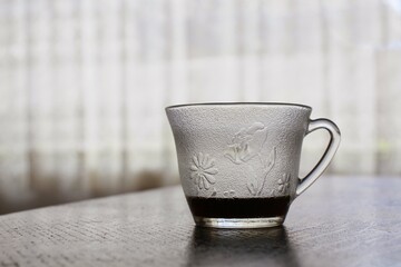 Taza de vidrio grabado en alto relieve, con un poco de café sobre una mesa