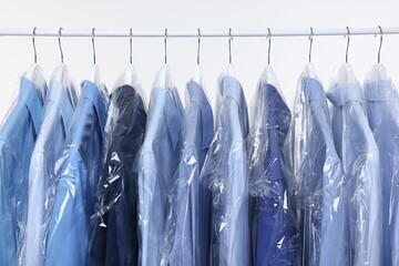 Dry-cleaning service. Many different clothes in plastic bags hanging on rack against white...