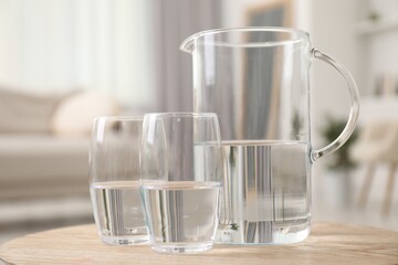 Jug and glasses with clear water on wooden table indoors, closeup