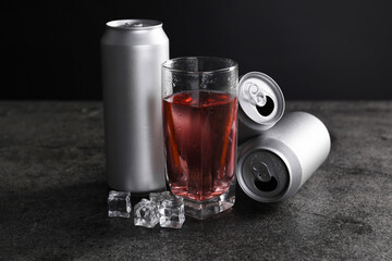 Energy drink in glass, aluminium cans and ice cubes on grey table
