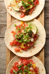 Delicious tacos with vegetables, green onion, lime and ketchup on wooden table, top view