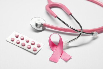 Pink ribbon, stethoscope and pills on white background, closeup. Breast cancer awareness