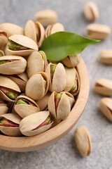 Delicious pistachios in bowl on grey textured table, closeup