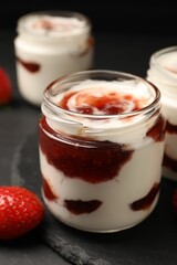 Tasty yoghurt with jam and strawberry on black table, closeup