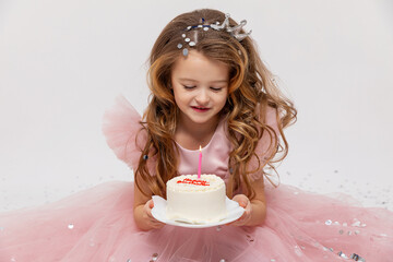 Cute little girl in a pink princess dress makes a wish and blows out the candles on the birthday...