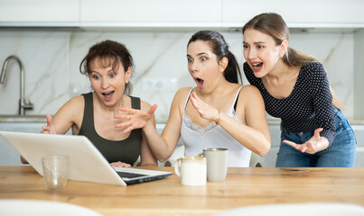 Three happy middle-aged woman expressing joy for winning standing by laptop at home