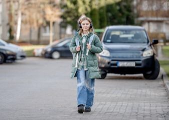Obraz premium Sweet Girl Walks Down Street In Early Spring, Listening To Music In Headphones