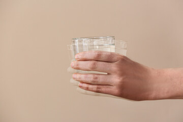 Trembling hand with glass of water on beige background. Parkinson's Awareness Month