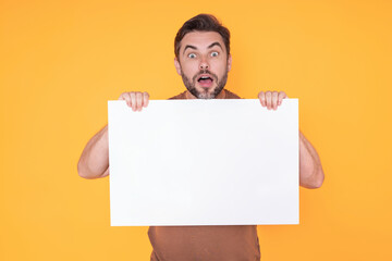 Handsome amazed surprised man holding empty board and pointing finger on studio. Amazed guy showing...