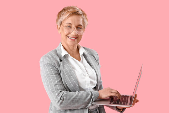 Mature female programmer working with laptop on pink background