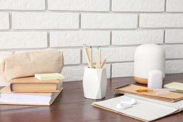 Holder with different stationery and modern earphones on wooden desk