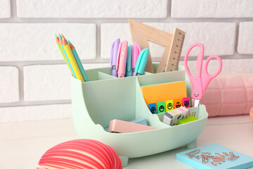 Holder with different stationery on light wooden desk, closeup