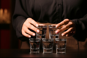 Fototapeta na wymiar Female bartender with shots of cold vodka on table in bar, closeup