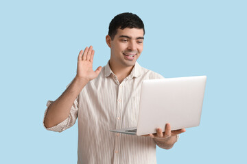 Happy young man with laptop video chatting on blue background