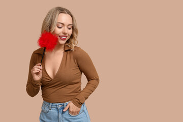 Beautiful young woman with feather stick on beige background