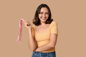 Beautiful young woman with whip on beige background