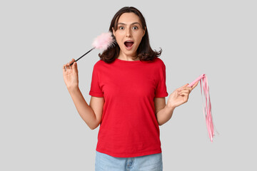 Shocked young woman with different sex toys on grey background
