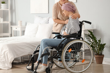 Fototapeta na wymiar Young woman after chemotherapy in wheelchair with her mother hugging at home. Stomach cancer concept