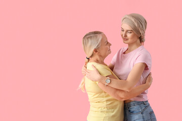 Young woman after chemotherapy with her mother hugging on pink background. Stomach cancer concept