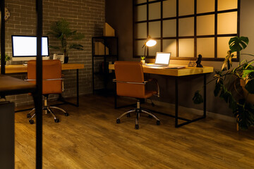 Interior of dark office with desks and glowing lamp at night