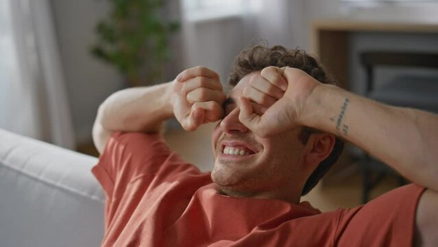 Closeup lazy guy falling on coach stretching arms at home. Carefree man resting
